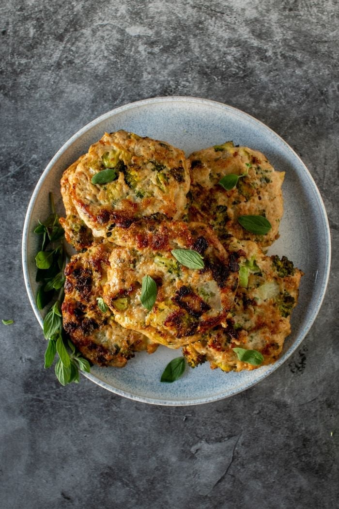 stack of chicken fritters with broccoli and cheese are piled on a plate